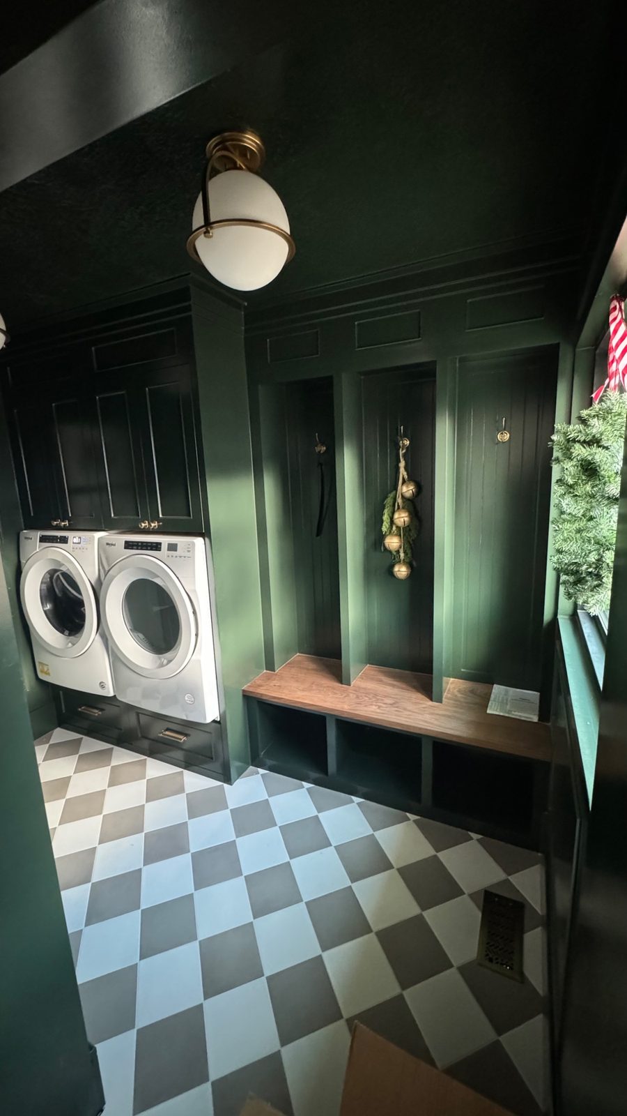 Bountiful laundry and mudroom — deep green paneling, walnut bench, mudroom cubbies, brass fixture